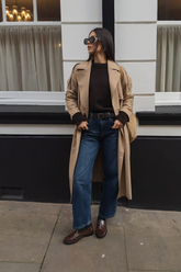 a lady in a black sweater, a long trench coat and a pair of jeans